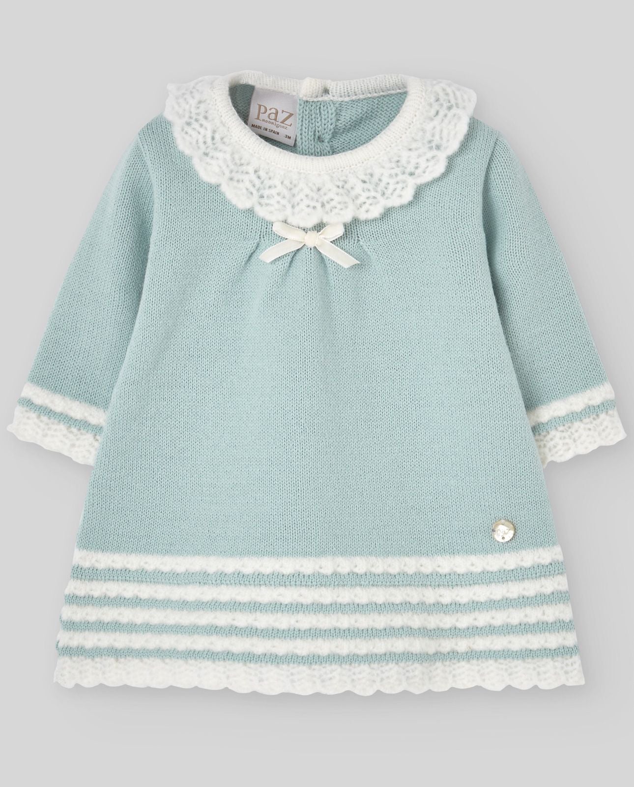 A baby girl is wearing a blue knitted dress with a white lace collar.;A baby girl is wearing a blue and white knitted dress with a white lace collar.