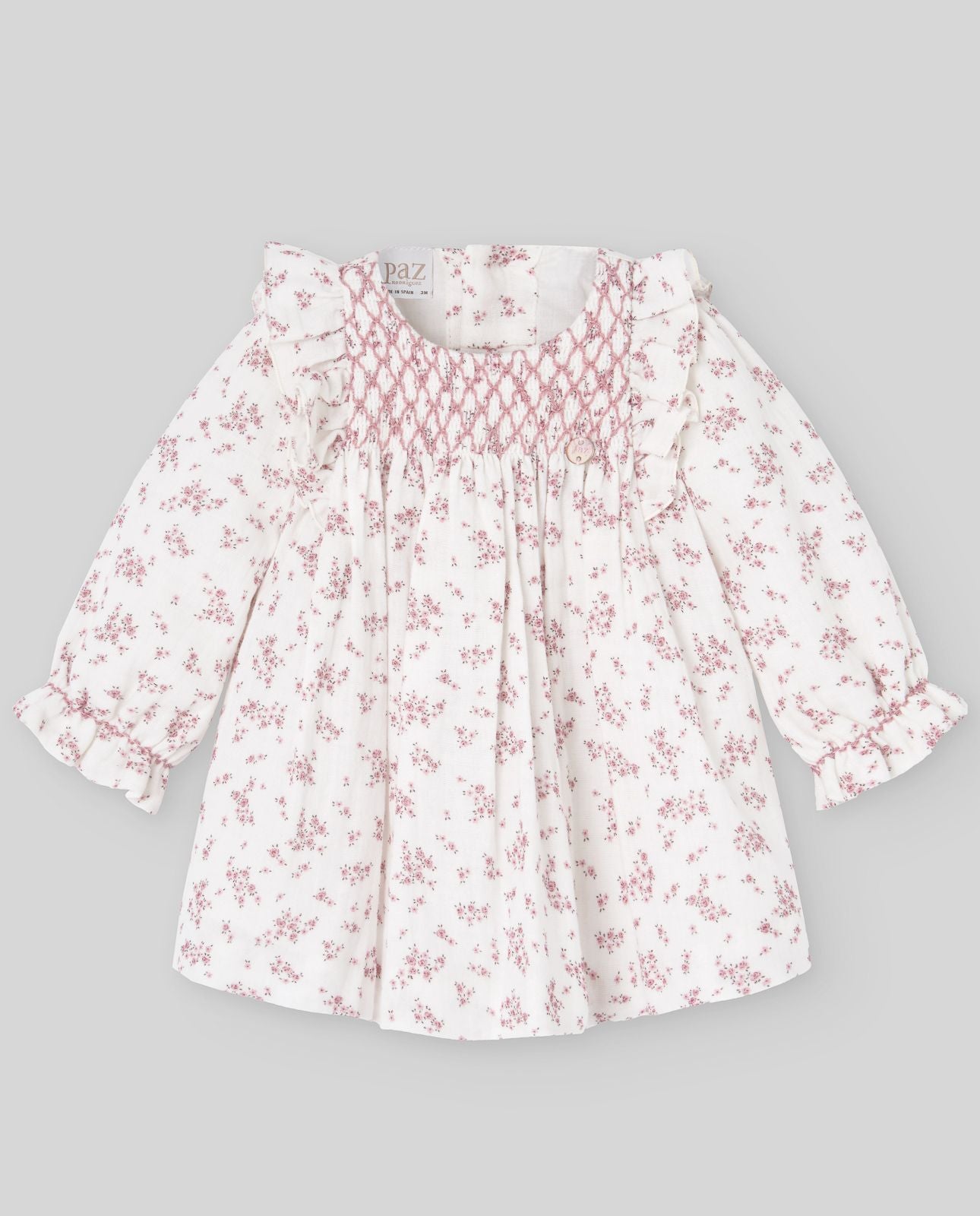 A baby girl is wearing a white dress with pink flowers on it.;A baby girl is wearing a white dress with pink flowers on it.