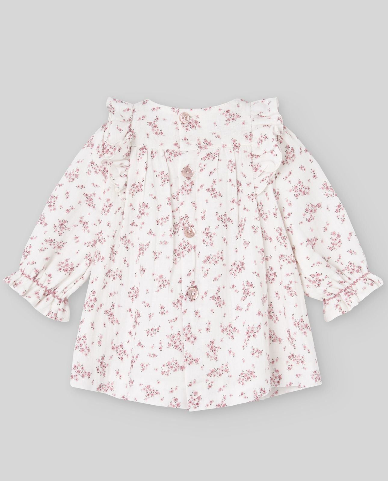 A baby girl is wearing a white dress with pink flowers on it.;A baby girl is wearing a white dress with pink flowers on it.