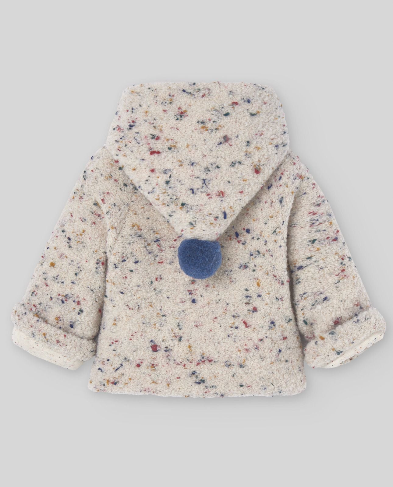 A baby is wearing a white jacket with a hood.;The back of a white jacket with a blue pom pom on the hood.