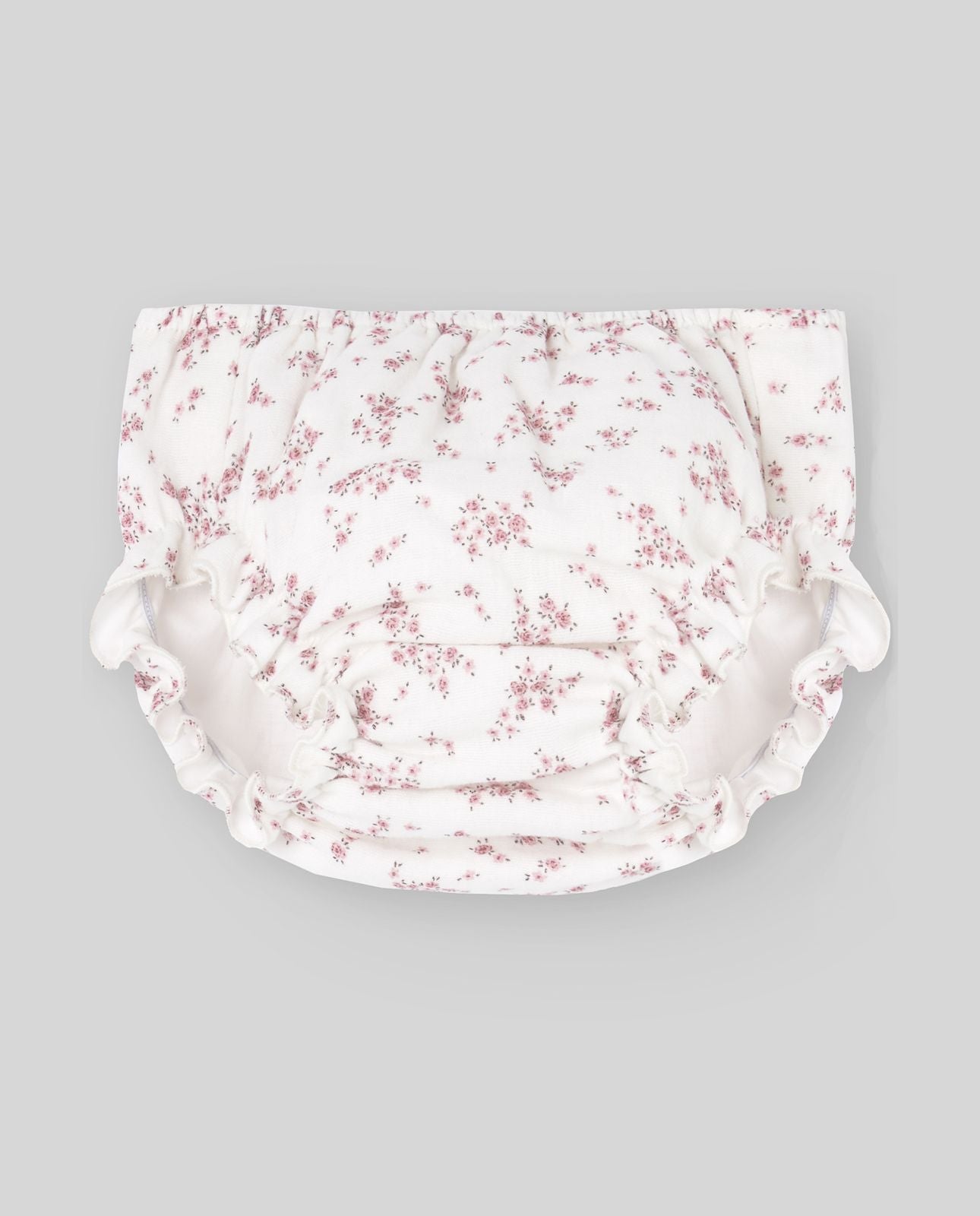 A baby girl is wearing a white dress with pink flowers on it.;A baby girl is wearing a white dress with pink flowers on it.