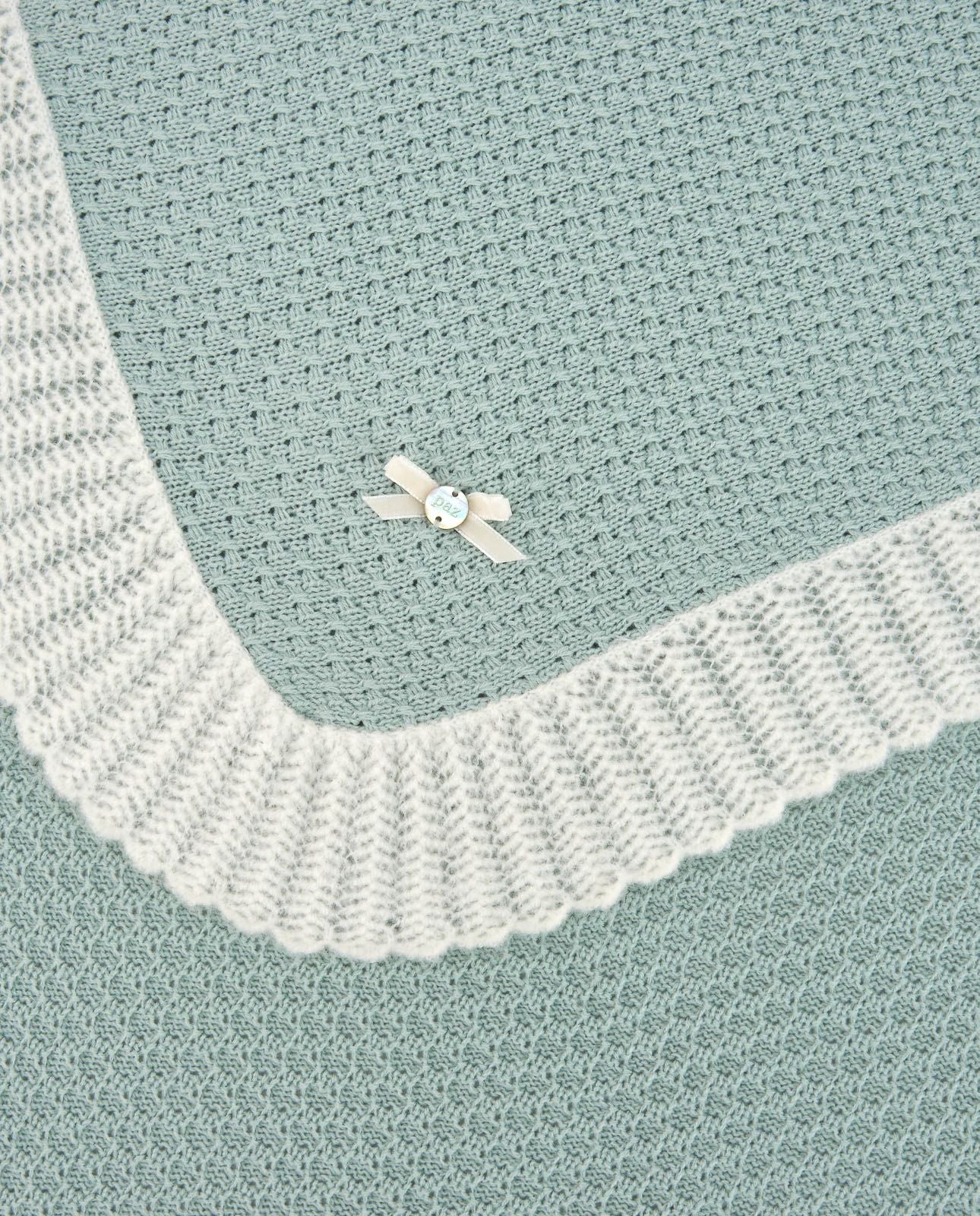 A close up of a knitted blanket with a flower on it.;A blue and white blanket with a bow on it