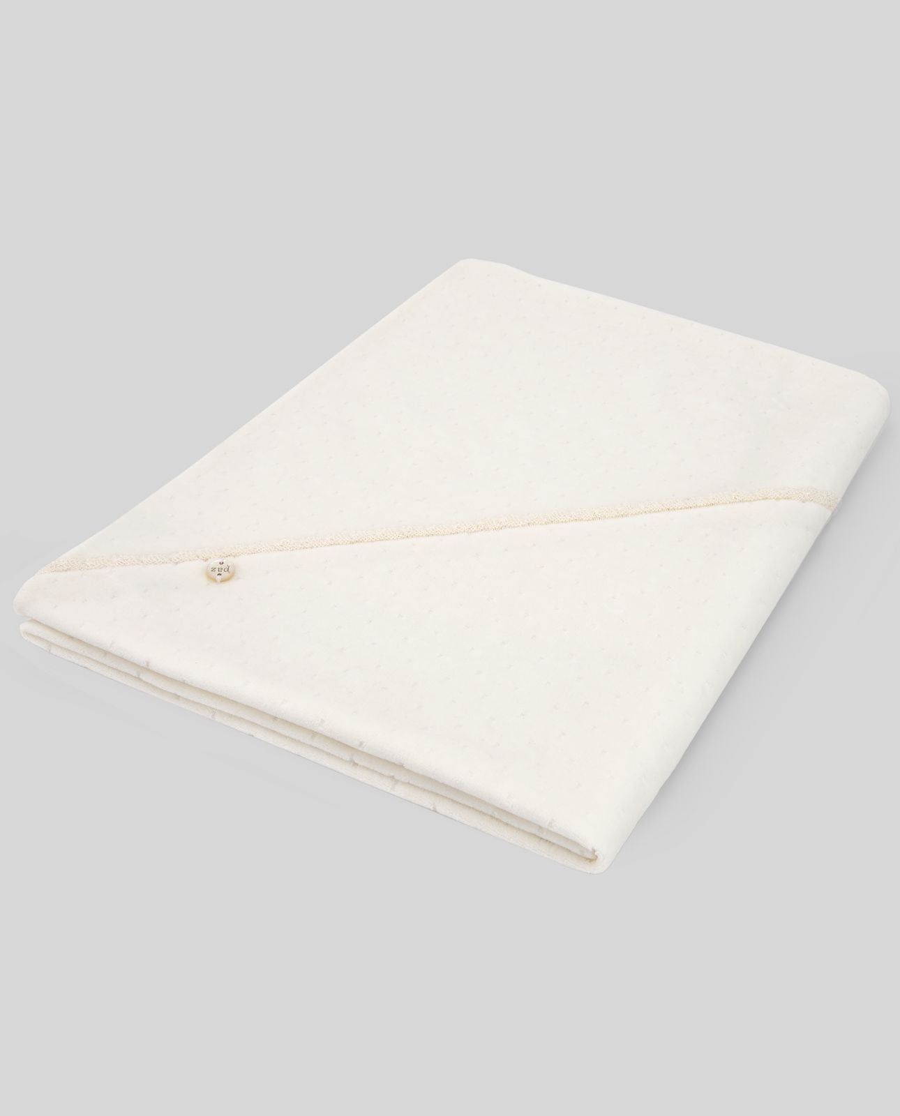 A white blanket with a pearl embroidered border is laying on a white surface.;A close up of a white cloth with a lace trim and a button.