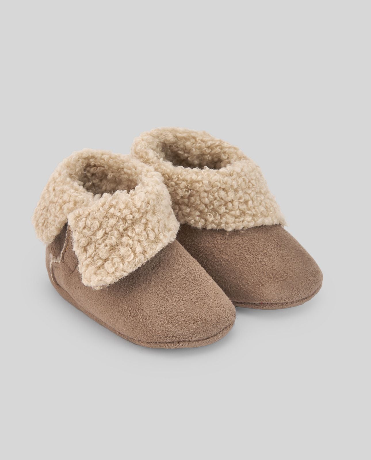 A pair of brown slippers with a furry cuff on a white background.;A pair of brown baby shoes with a furry collar on a white background.