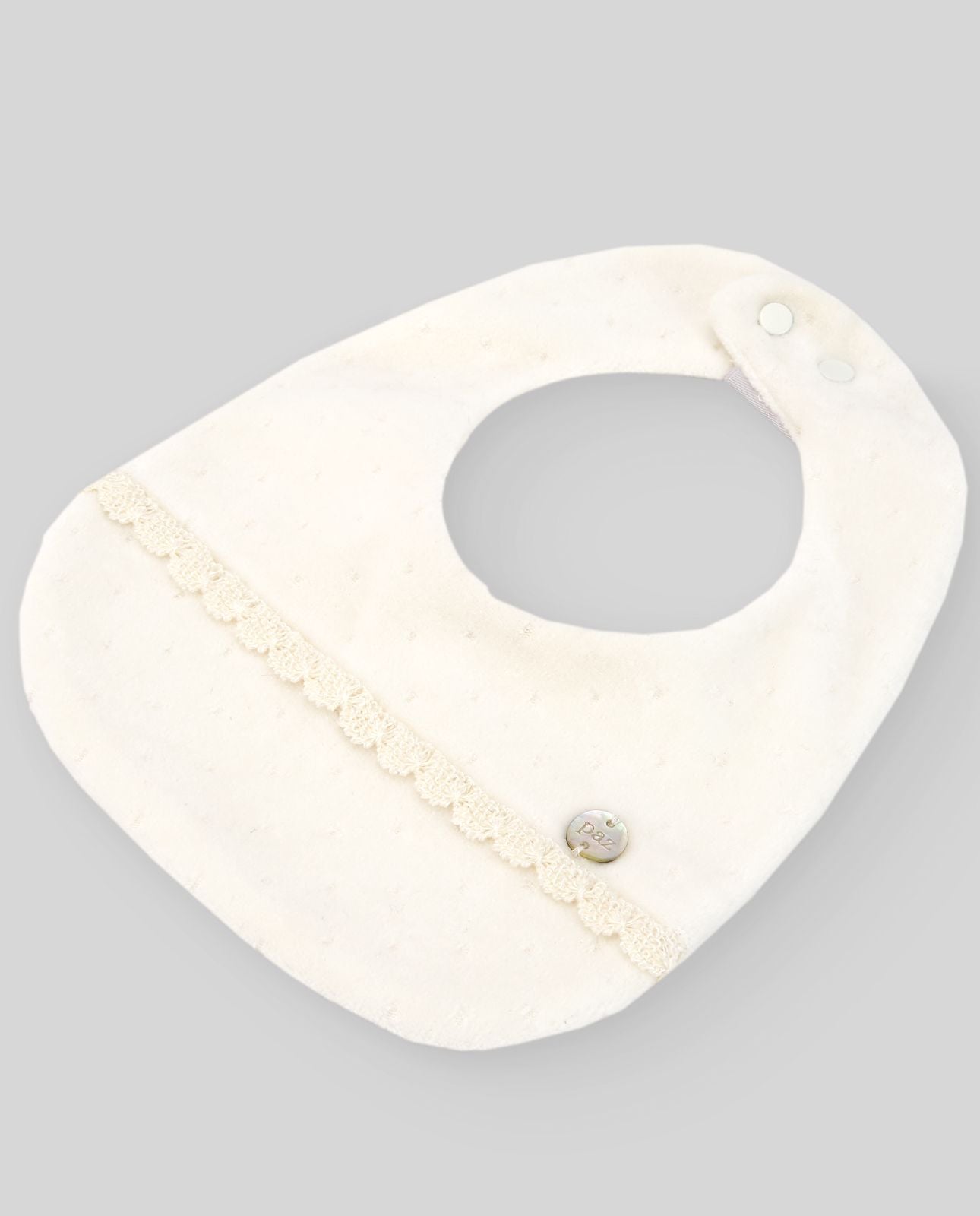 A white bib with a lace trim and a button on it is on a white surface.;A white baby bib with a button on it