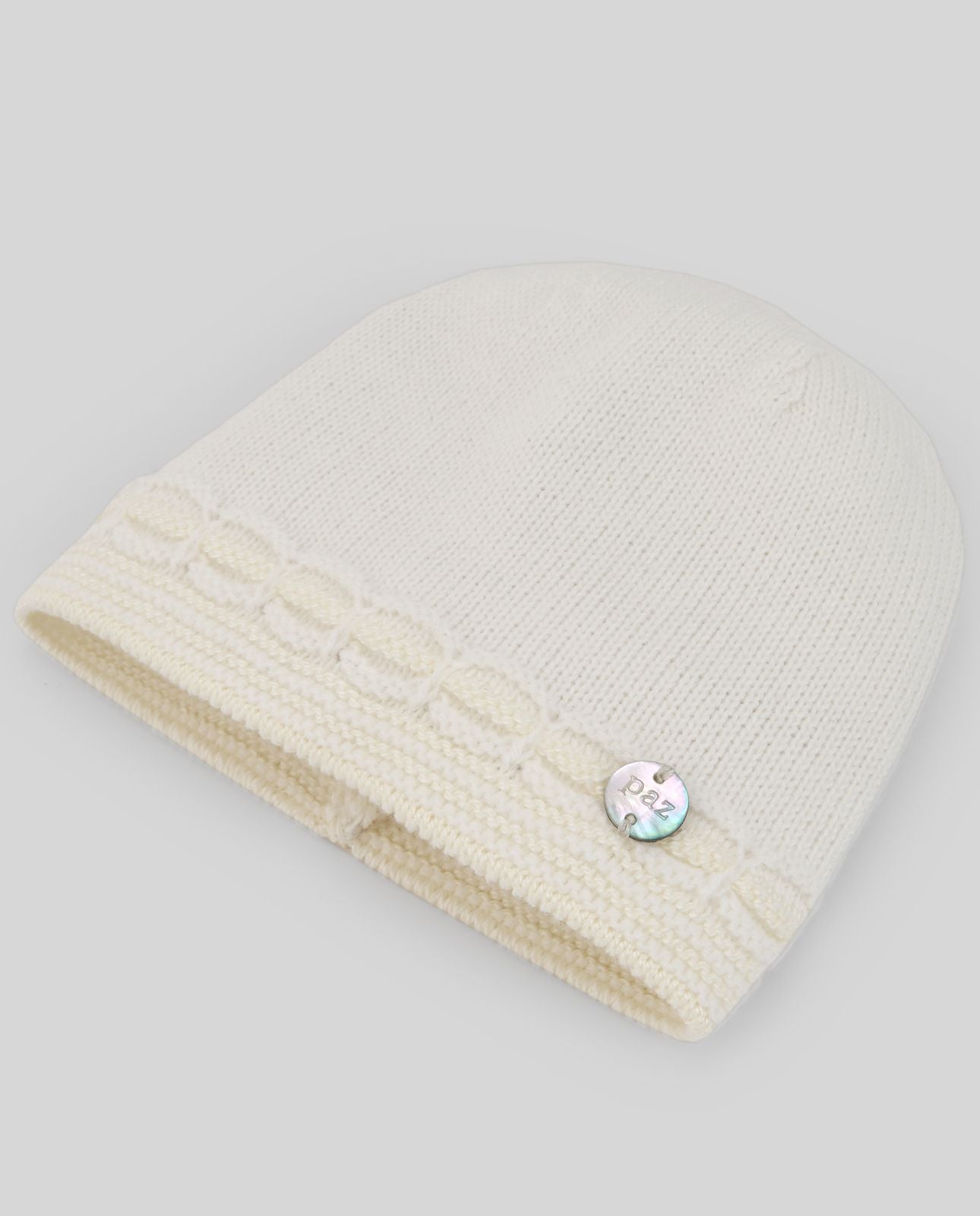 A white knitted hat with a button on the side.;A white beanie with a rhinestone on it
