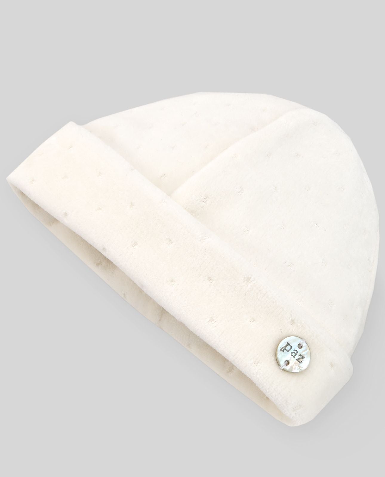 A white baby hat with a button on the side.;A white beanie with a button on the side on a white background.