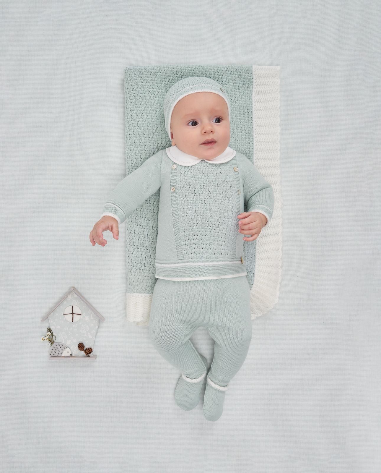 A baby is wearing a green sweater with a white collar.;A baby is wearing a green sweater with a white collar.;A pair of knitted baby pants with feet on a white background.;A pair of baby pants with feet on a white background.;A baby is laying on a bed wearing a hat and a sweater.