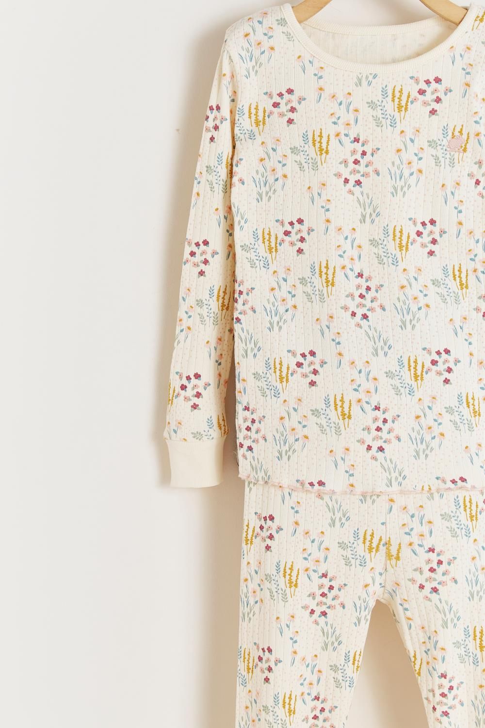 A white shirt with a floral print is hanging on a wooden hanger.;A close up of a fabric with a floral pattern on it.;A white pajama set with a floral print is hanging on a hanger.;A white pajama set with a floral pattern is hanging on a hanger.;A pair of white pants with a floral print is hanging on a wooden hanger.;A white pajama set with a floral print is hanging on a hanger.