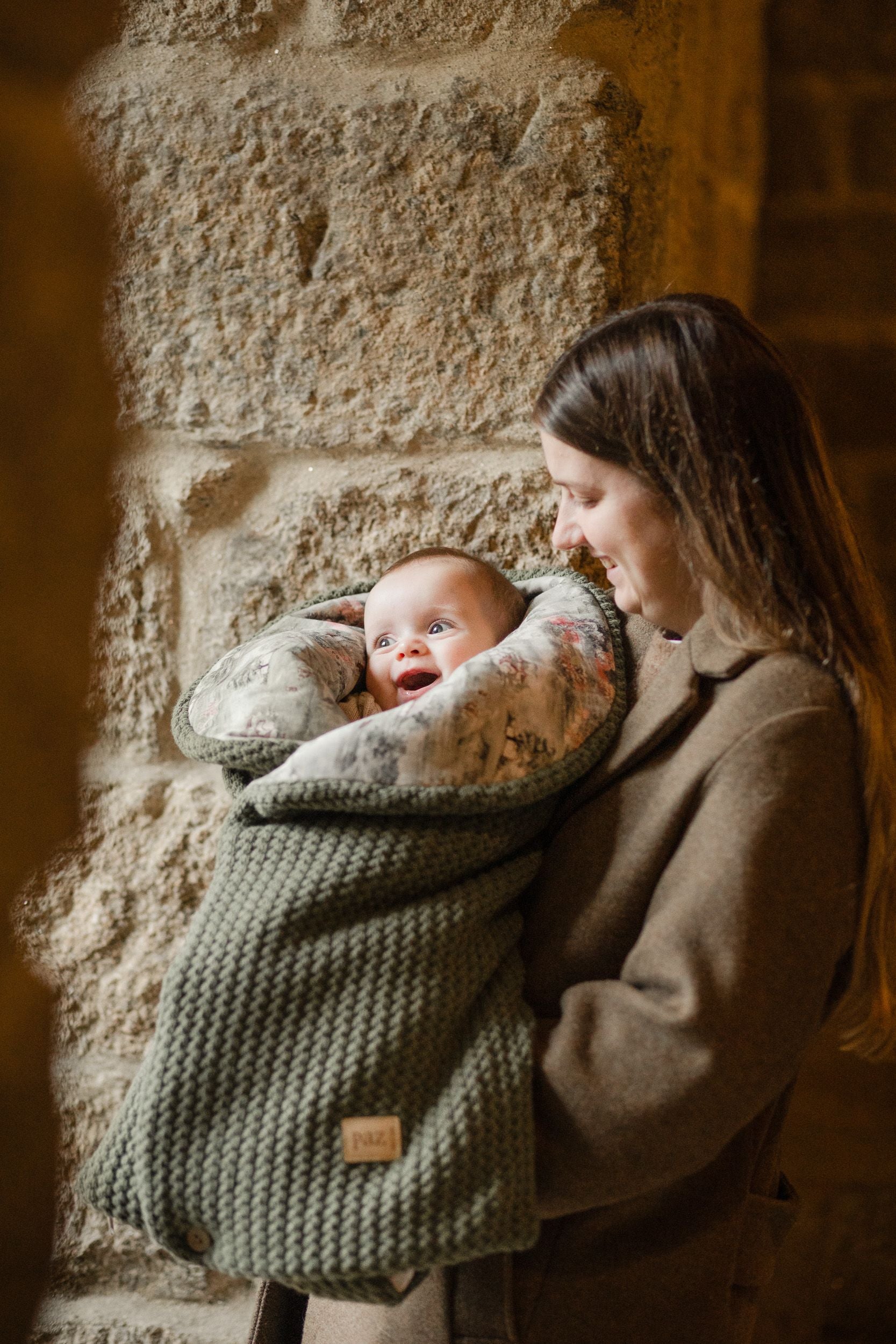 A woman is holding a baby wrapped in a blanket.;A green sleeping bag with a white polka dot lining