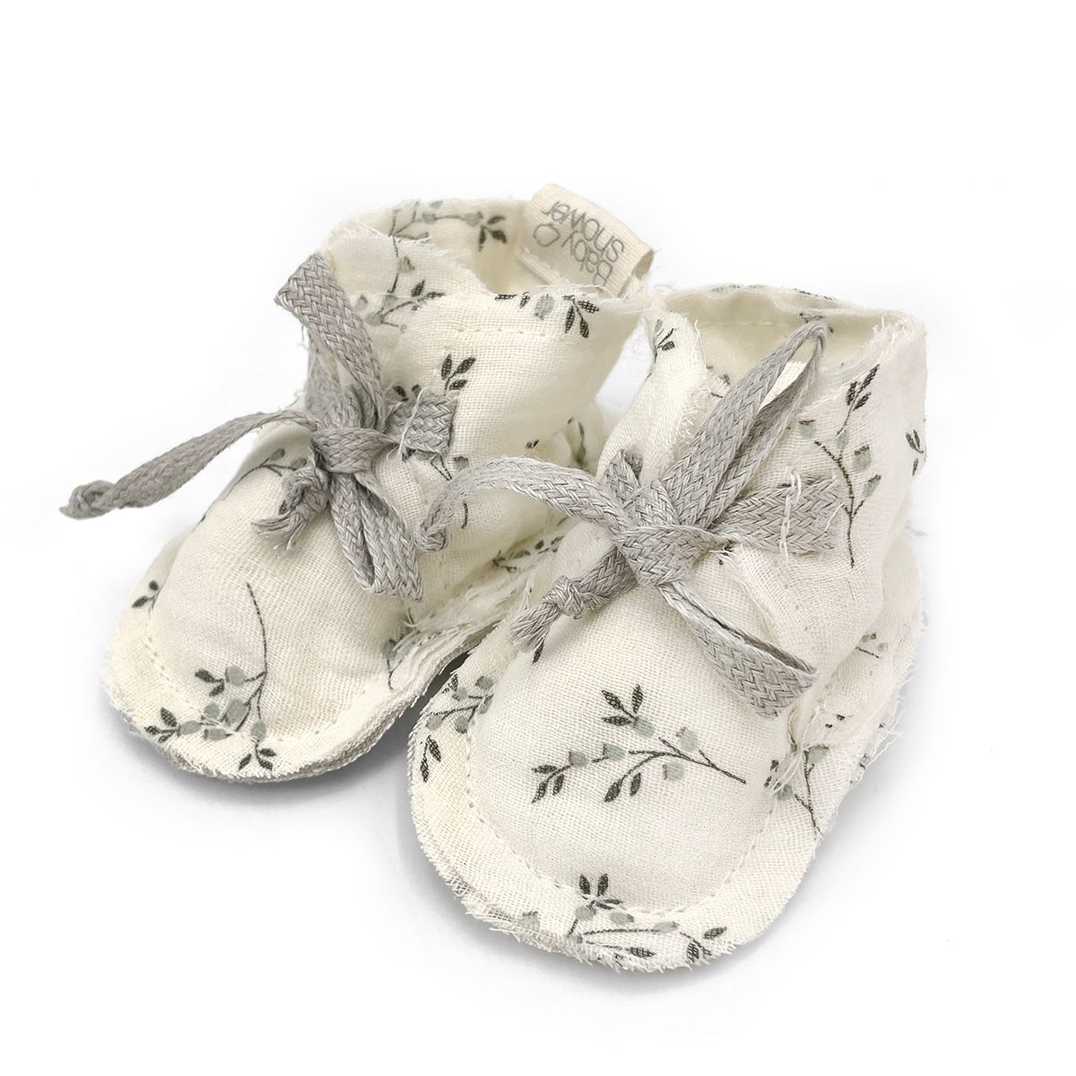 A pair of white baby shoes with a silver ribbon on a white background.