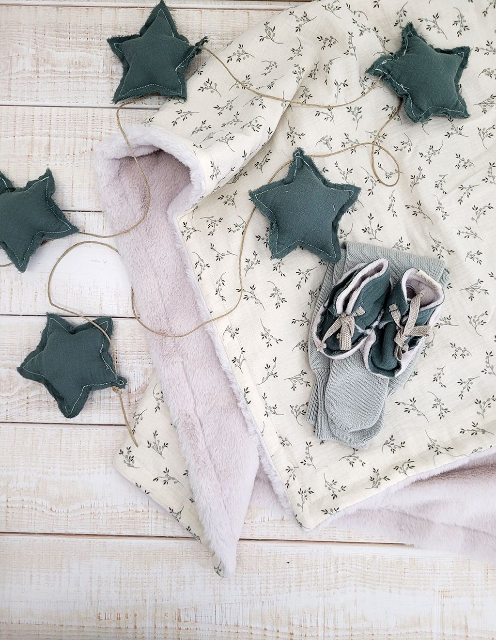 A baby blanket and a pair of shoes are sitting on a wooden table.
