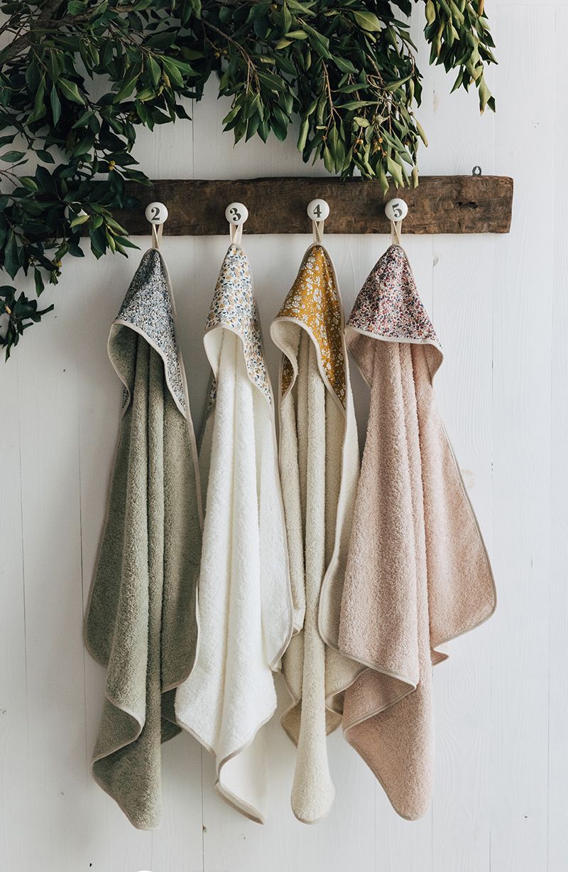 Four towels with hoods are hanging on a wooden rack.;A white towel with a floral pattern on the hood;A pink towel with a floral pattern on the hood;A white towel with a hood on it;A blanket with a hood is wrapped in a towel on a white background.;A white towel with a hood on it;A white towel with a hood on it;A white towel with a hood and flowers on it;A white towel with a floral pattern on the hood;A gray towel with a hood and polka dots on it