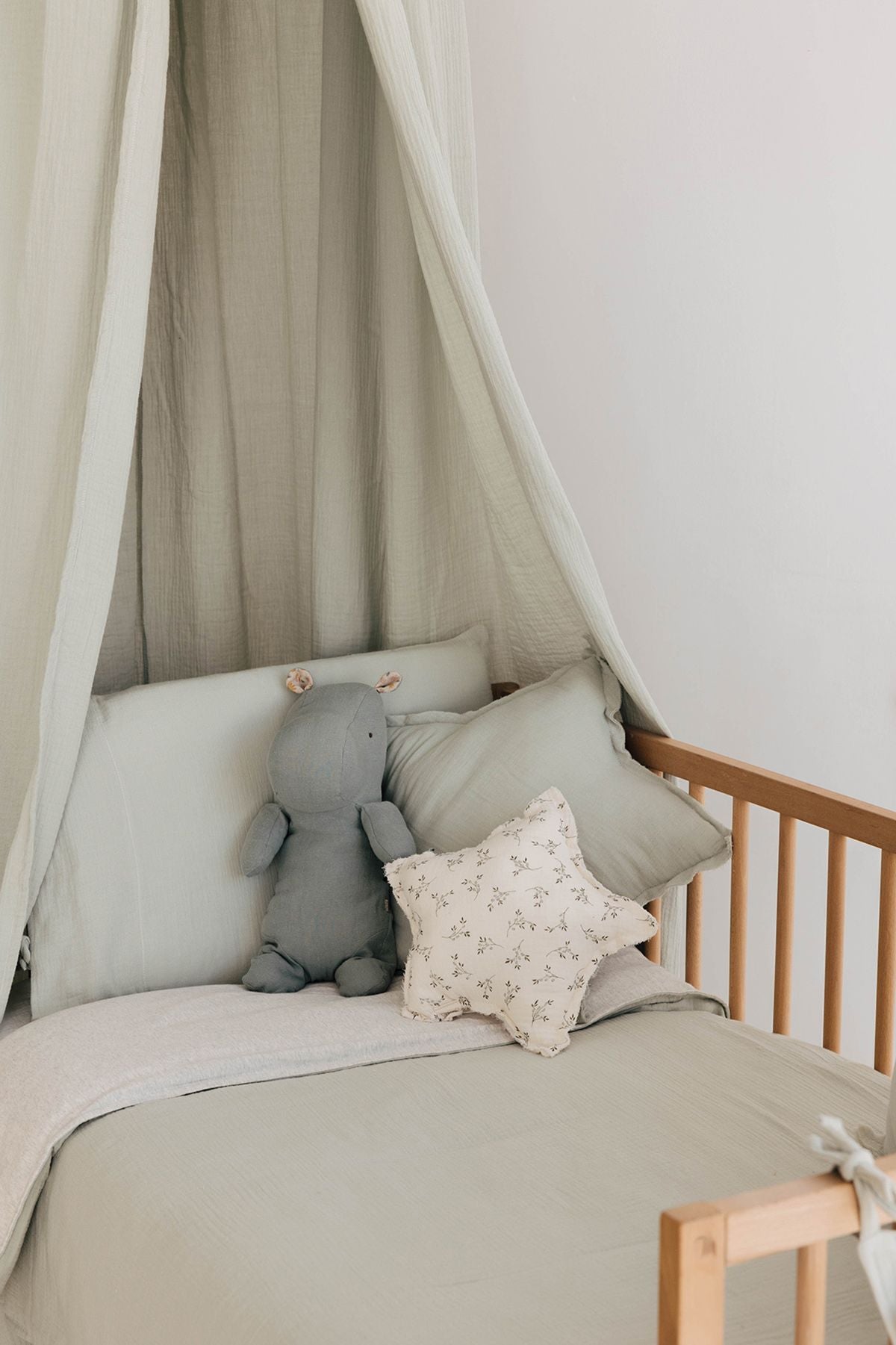 A newborn baby wrapped in a white blanket is sleeping on a bed.;A bed with a canopy , pillows and a teddy bear on it.