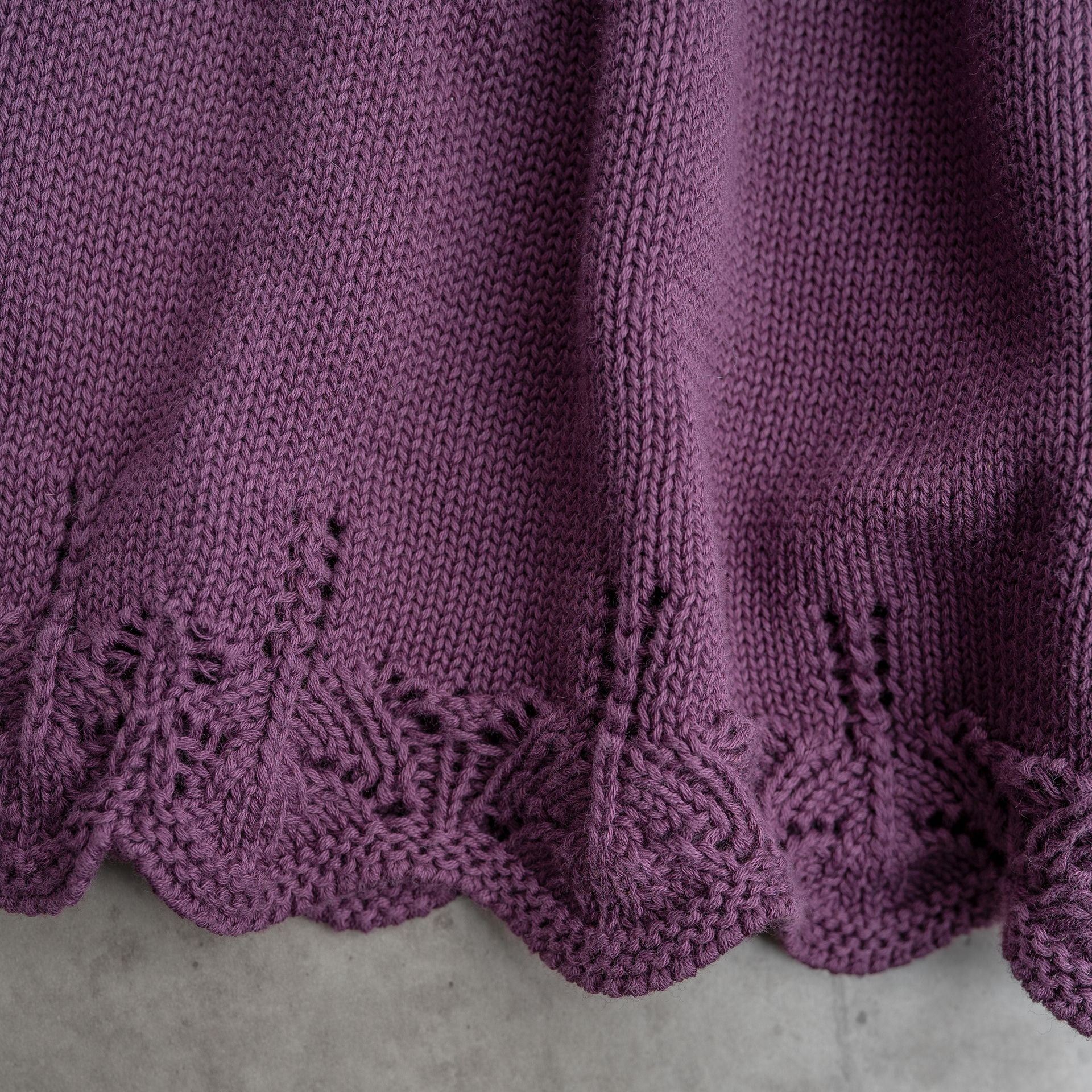 A close up of a purple knitted blanket with a lace trim.;A purple knitted skirt is on a white background.;A little girl is standing on a dirt road in the woods.