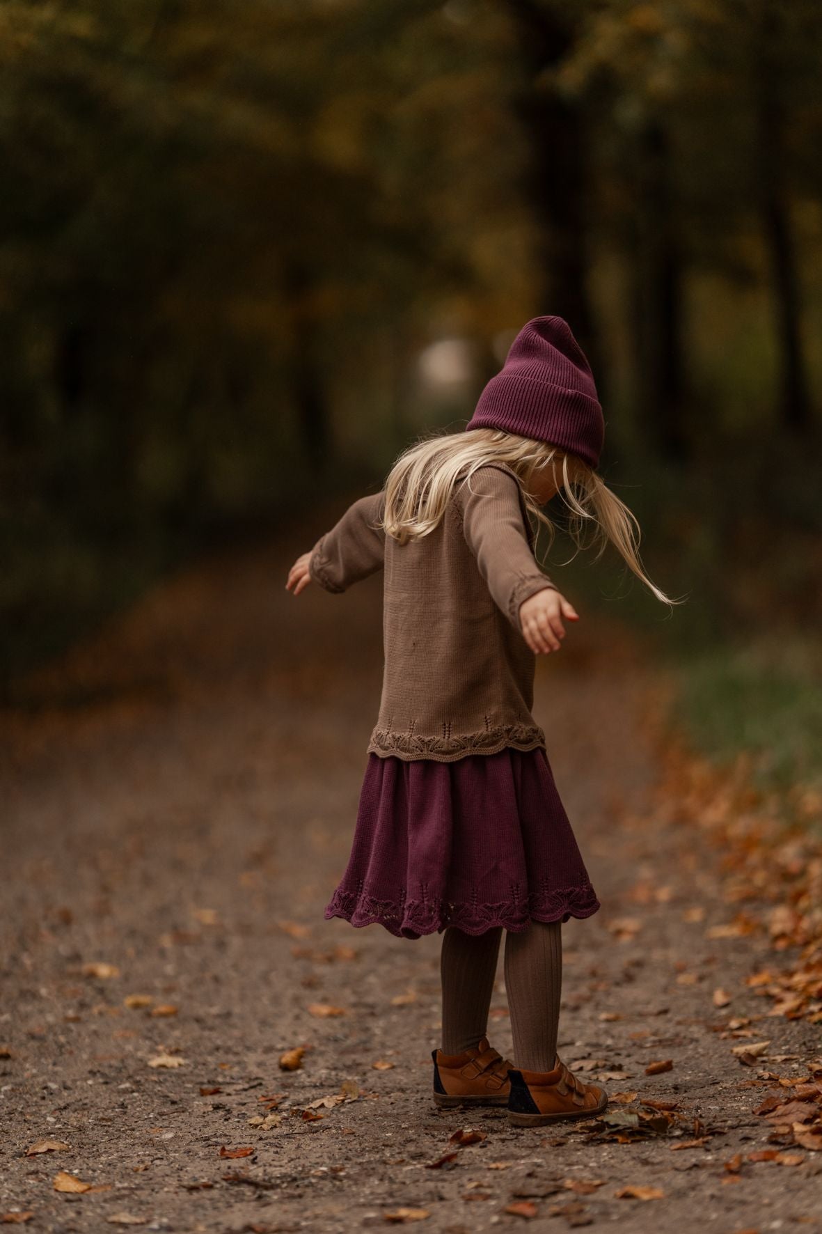 A close up of a purple knitted blanket with a lace trim.;A purple knitted skirt is on a white background.;A little girl is standing on a dirt road in the woods.