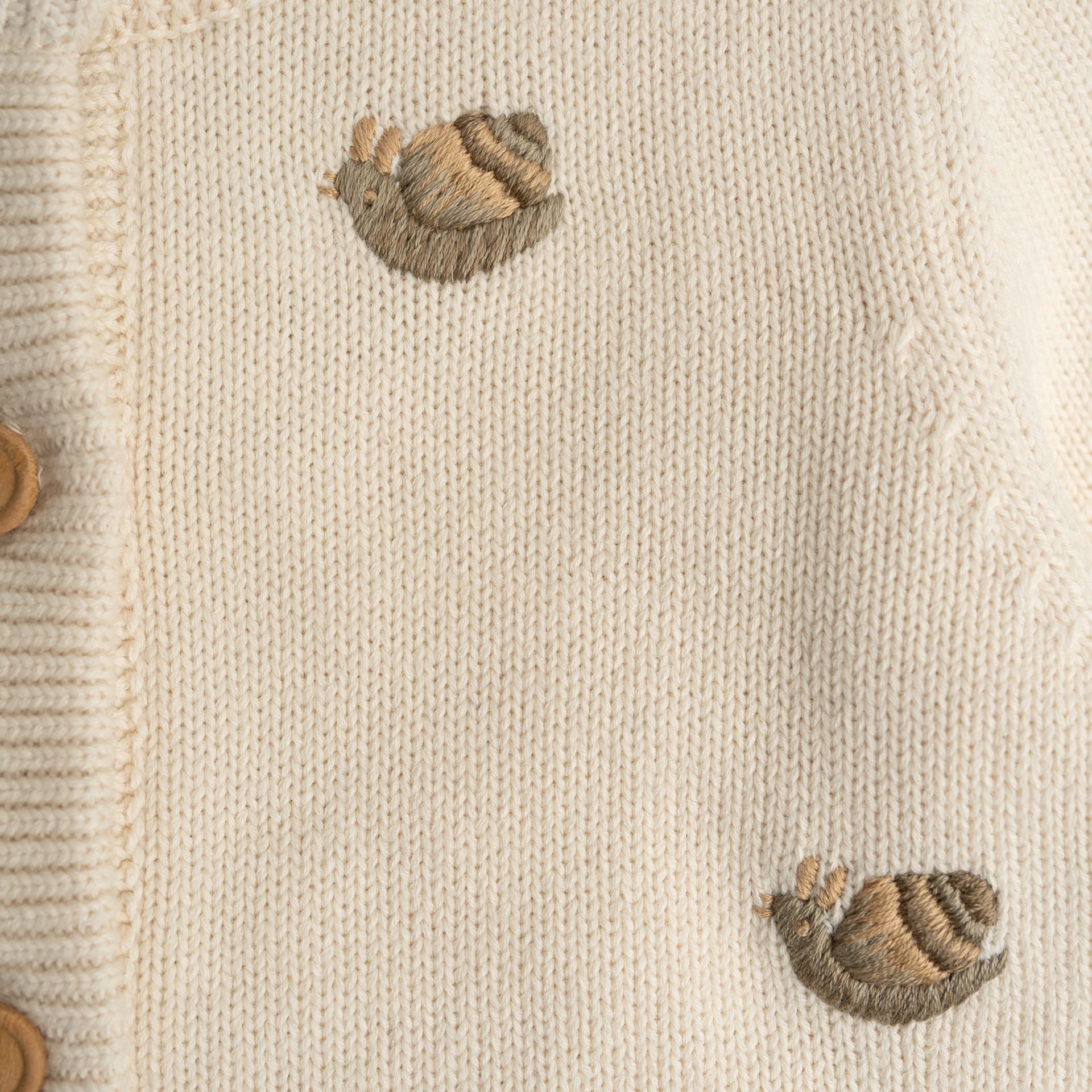 A young boy is sitting on a chair wearing a white sweater.;A white cardigan with squirrels embroidered on it;The back of a white sweater with long sleeves on a white background.;A close up of a sweater with a sheep embroidered on it.