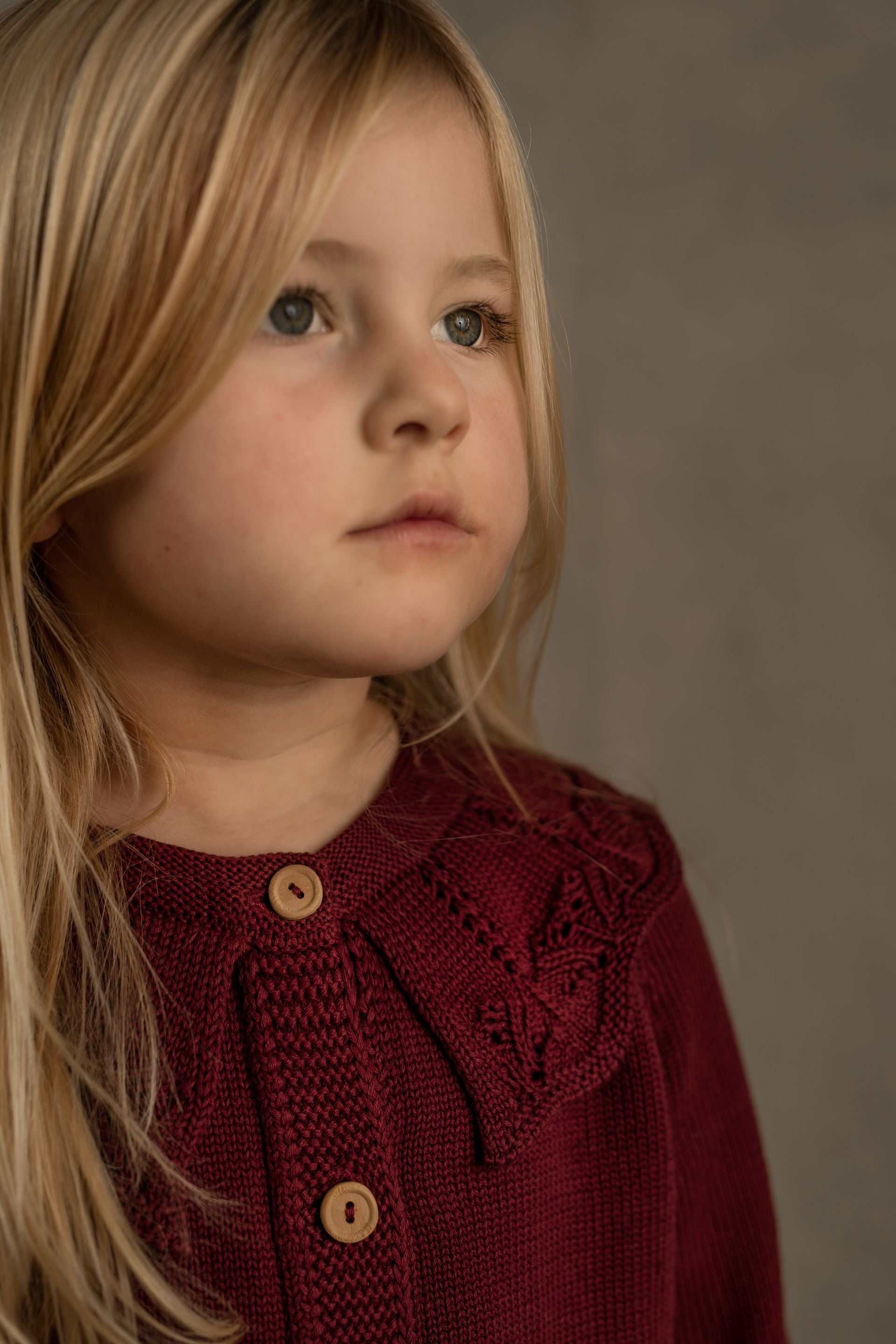 A baby girl is wearing a burgundy cardigan with ruffles and buttons.;A red sweater with long sleeves and a ruffled collar;A close up of a purple sweater with wooden buttons.;A little girl is wearing a red sweater and looking at the camera.