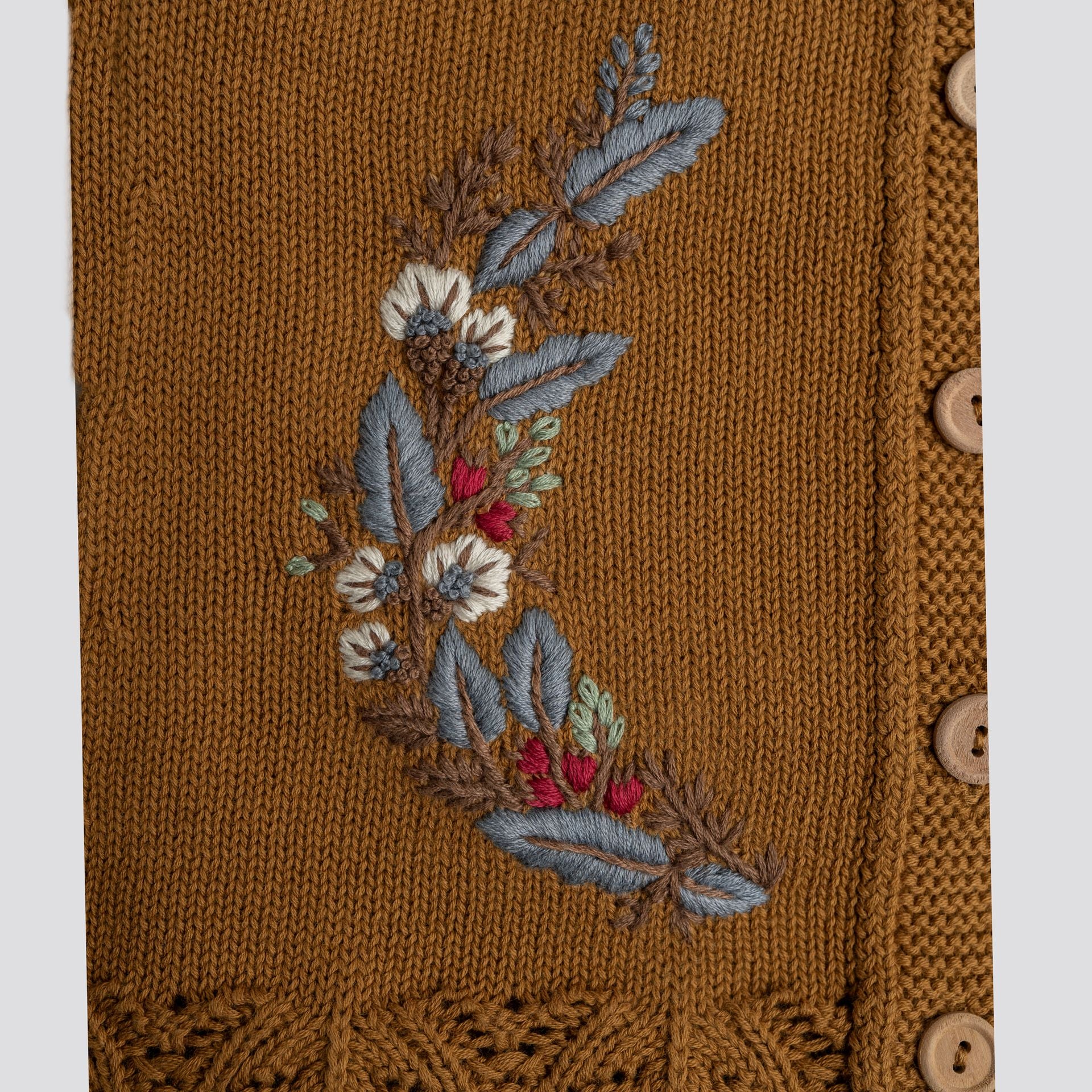 A little girl wearing a brown sweater and a white hat is standing in the snow.;A baby girl is wearing a brown cardigan with embroidery on it.;A close up of a sweater with a floral embroidery on it.;A close up of a sweater with a flower embroidered on it.